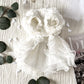 The underside of a white dog wedding dress with pearls and a tulle skirt on a textured white background, surrounded by gold earrings, white hearts, plant leaves and a magazine corner.