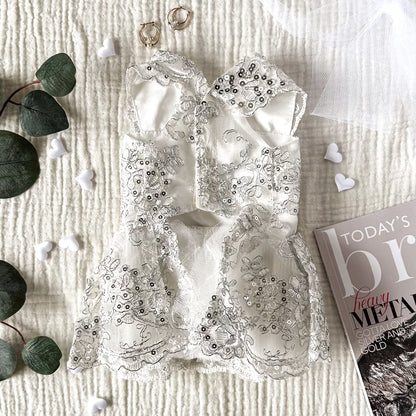 The underside of a white dog wedding dress with silver sequins on a white textured background, surrounded by plant leaves, white hearts, gold earrings and a magazine corner.