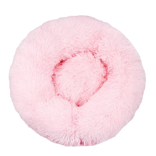 A light pink plush dog bed shaped like a donut, offering a comfortable and secure space for small dogs to curl up and relax.