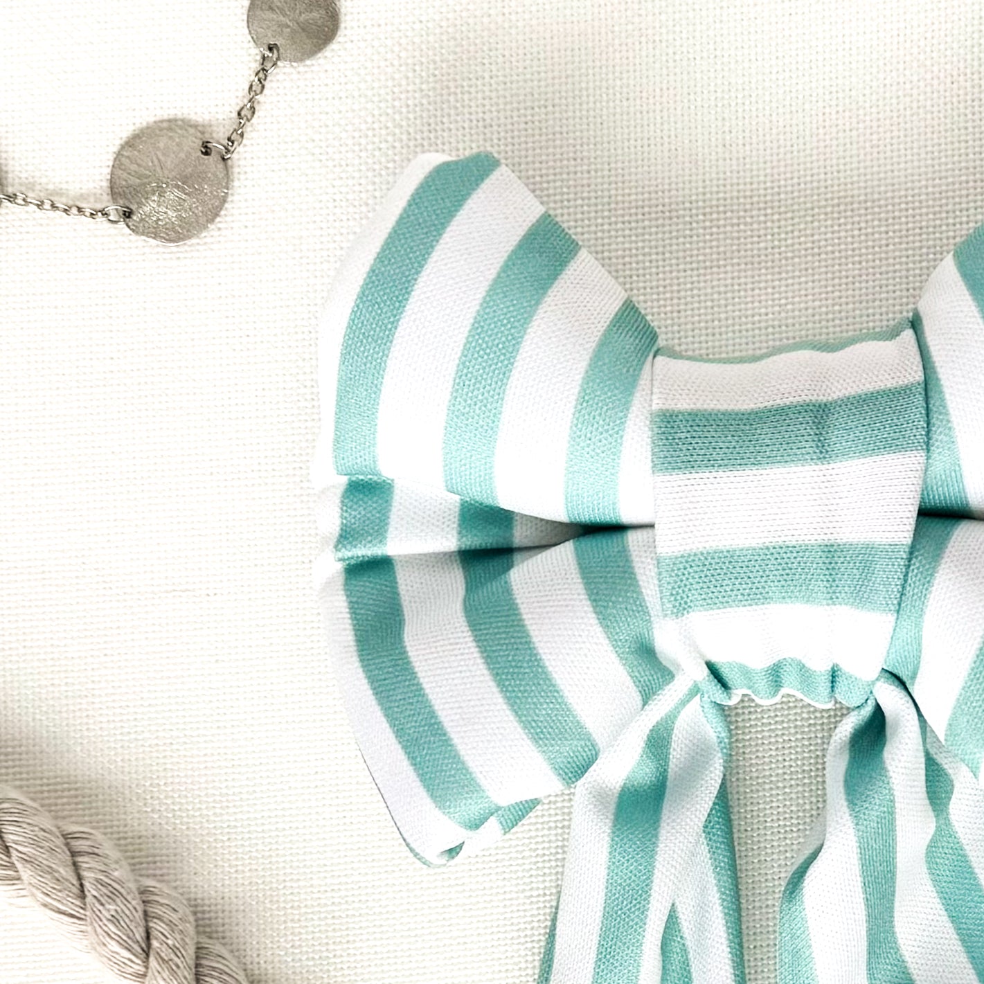 Close up view of a turquoise and white striped dog sailor bow.