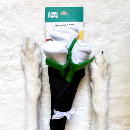 A black and white bouquet of roses plush dog toy surrounded by 2 dog paws/legs.